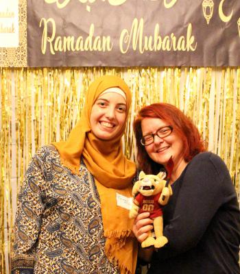 Two women friends posing in front of a Ramadan Mubarak sign with stuffed animal 