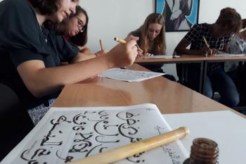 Students work on learning calligraphy. In the foreground is a student's example