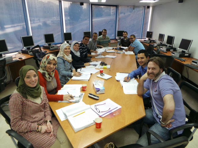 A group of graduate students sit around a table and smile at the camera, there are pens and papers in front of them